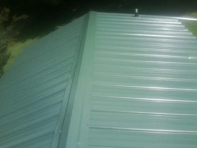 New green metal panels meeting at the ridge of a roof — Flat Roof Repair work by our crew in Clyde