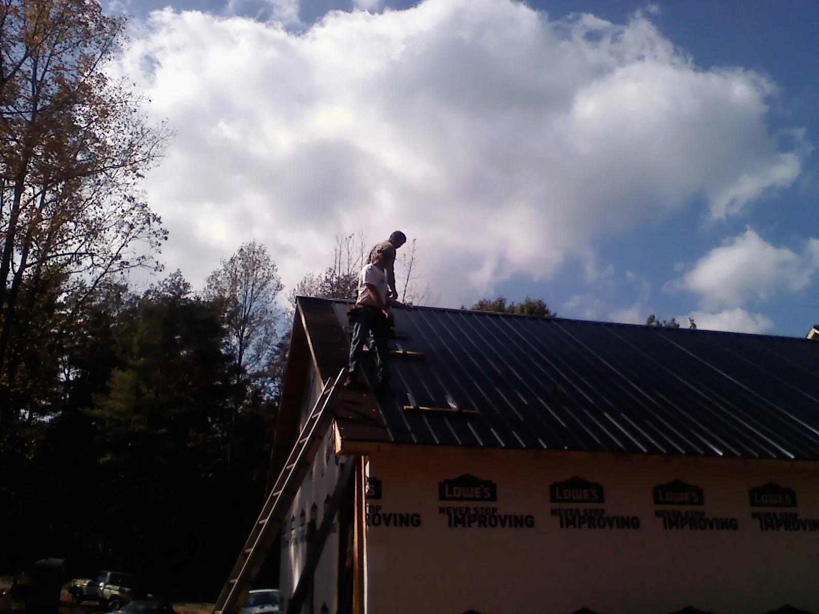 Roofer fastening dark metal panels high against a cloudy sky, from a Roof Inspection job in Clyde